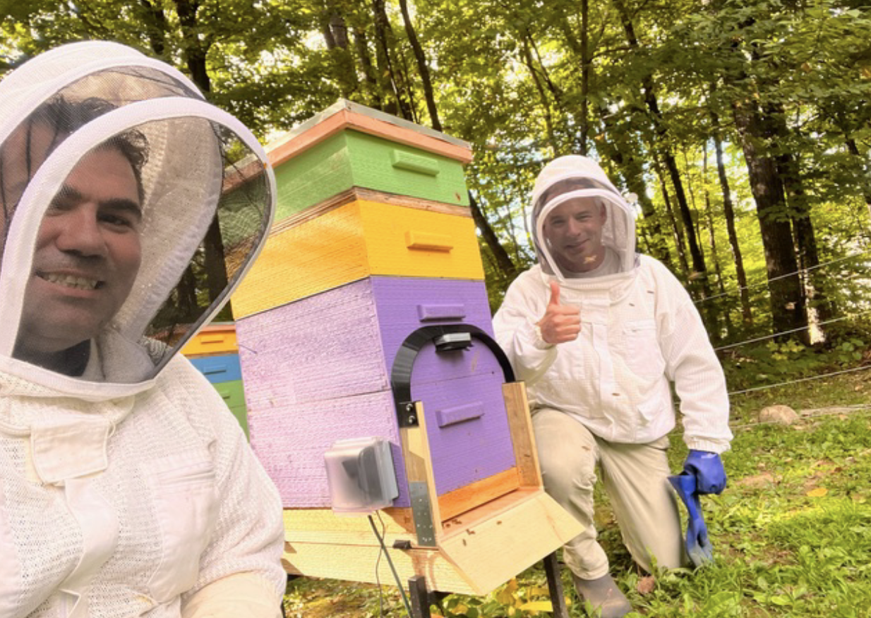 Akin Tatoglu and Eric Rosow smiling beside a colorful hive with a mounted sensor